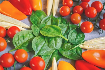Variety of fresh organic vegetables tomatoes corn peppers and spinach on a beautiful background, top view, selective focus.の写真素材