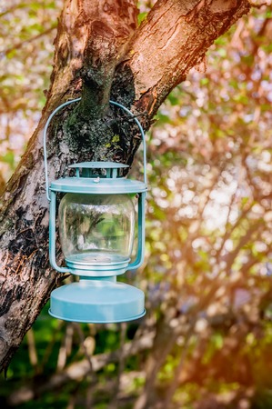 Decorative blue glass Lamp with candles hanging on a tree in the garden.の写真素材