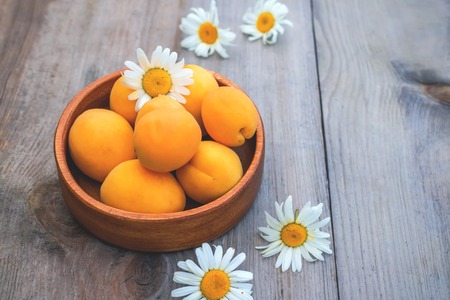 Ripe Golden apricots in wooden bowl on wooden background. Copy spaceの写真素材