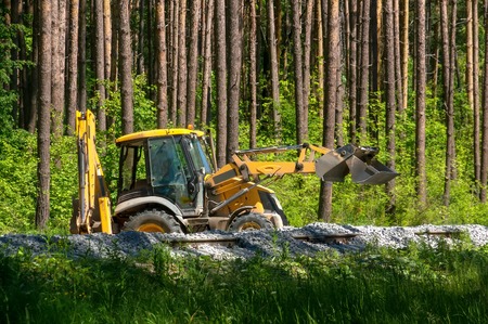 Yellow excavator pours gravel on the construction of the railway in the forest.の写真素材