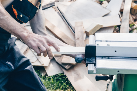 The master sharpens the wooden panel with an electric sander on a Sunny day in the garden. Close up.の写真素材