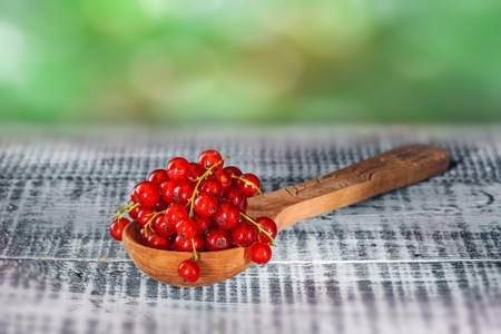 Ripe red currant berries in wooden spoon on wooden background. Copy spaceの写真素材