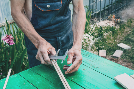 The master sharpens the wooden panel with an electric grinder on a Sunny day in the garden. Dimensioningの写真素材