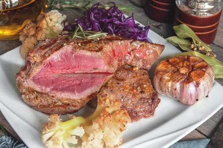 Steak with blood medium rare with a side dish of tomatoes and vegetables with spinach sauteed in a homemade pan on a wooden table.の写真素材