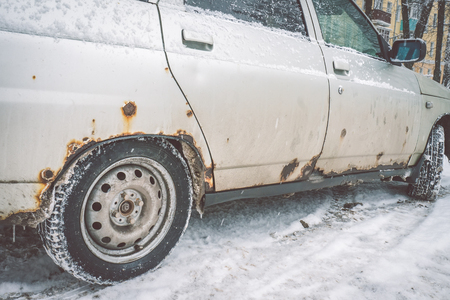 The bottom of the doors and the bottom of the white car in winter is covered with a caustic iron defect. The concept of car damage by chemical reagents for cleaning roads from snow.の写真素材