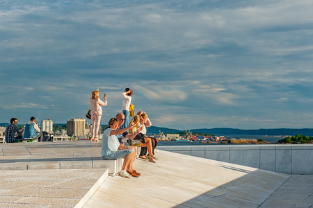 Norway, Oslo August 1, 2013: Tourists take photos and admire the view of the Oslo panorama from the embankment of the Opera house at sunset. Editorialのeditorial素材