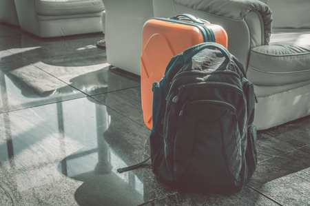 A black backpack and an orange suitcase stand in the hall at the reception. Luggage for travel.の写真素材