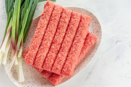 Chevapchichi is a national Balkan dish. Close up a row of fresh raw beef kebabs on a white...