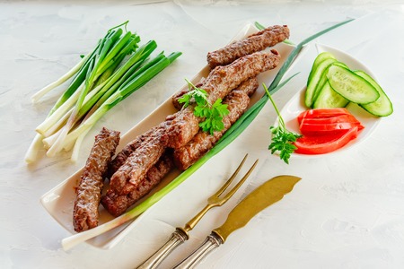 grilled Cevapcici is a Balkan national dish. Close the row of fried beef kebabs on a white rectangular dish with vegetables.の写真素材