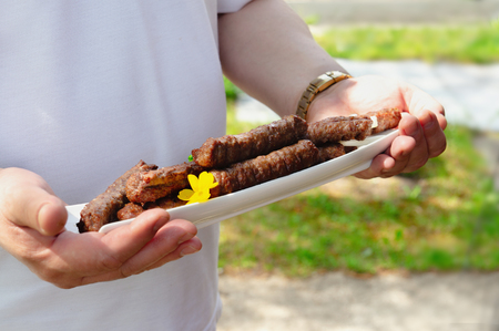 A man is holding hot fresh fried chevapchichi on a white dish. Grilled chevapchichi is a Balkan national dish. Close up.の写真素材
