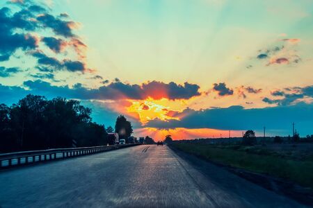 Highway with cars traveling on the sunset. Horizon line with the sun and storm clouds. Journeys. Selective focus.の写真素材