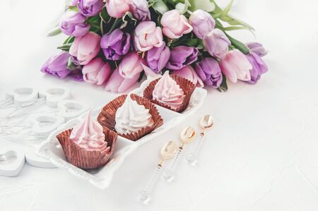 Pink homemade meringues on a white table with a bouquet of pink tulips. Gift set. Copy space.の写真素材