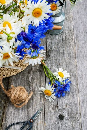 Making a bouquet of beautiful wild flowers of daisies and cornflowers on a wooden oldの写真素材