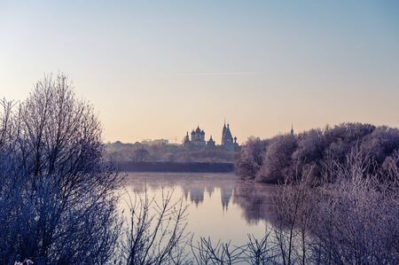 Winter landscape of temples of the city with sunset on the river Bank. The trees are covered with snow, the setting sun illuminates a beautiful mysterious landscape.の写真素材
