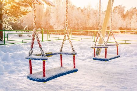 Bright Playground in the snow on a Sunny winter day. Children's swing swing on a winter Playground...