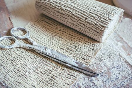Plaster bandage is prepared for dressing. The scissors are next to the plaster bandage.