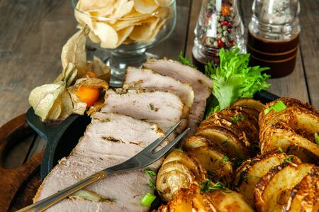 A piece of baked stuffed meat with potatoes and vegetables in a frying pan and a wooden Board.の写真素材
