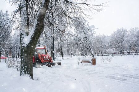 A red old tractor clears the street of snow in a snow storm. Street cleaning in winter.の写真素材
