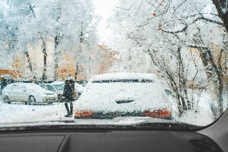 A pedestrian crosses the street in a snowstorm in front of the car. City street in winter in snow storm. Drops of icy rain on the windshield.の写真素材