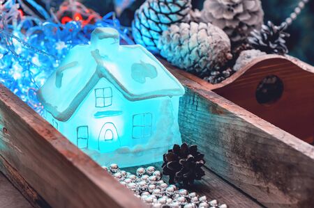 Festive Christmas decor. A luminous glass decorative transparent house lies in a box with Christmas...