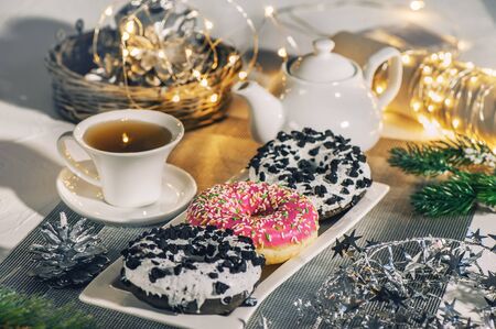 Pink and chocolate doughnuts lie on the Christmas table next to the tea in the teapot. New year celebration.の写真素材