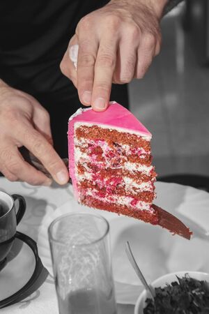 Hands waiter serves a piece of fruit cake in pink glaze on a family celebration-wedding, birthday.. Isolated on black background.の写真素材