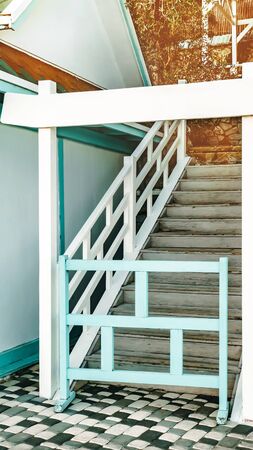 A white wooden staircase with wooden railings and handrails goes up. Stairs on the street. The...