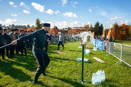 Moscow, Russia-October 1, 2016: descendants of the Cossacks at the fair and Cossack gathering. Cossacks in national clothes demonstrate the national martial art of juggling balls. The Cossack cuts the lid off the water bottle. Mastery of weapon.のeditorial素材