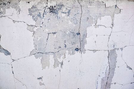 Gray cement wall with deep cracks from old age and precipitation.
