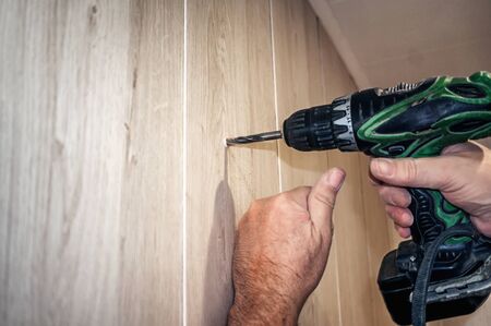 An electric drill makes a hole in a sheet of plywood. Authentic home renovation. Space for copying.の写真素材