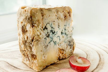 A piece of blue Stilton cheese on a wooden antique with large red grapes.の写真素材