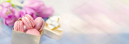 traditional French colored almonds lie in rows in a gift box on the background of a bouquet of flowers. Close-up, selective focus. Banner, copy space.の写真素材
