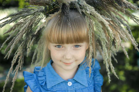 beautiful red-haired girl with freckles and a wreath of summer herbs on her head looks into the camera with blue eyes. Young beautiful girl 7-10 years old in nature.の写真素材