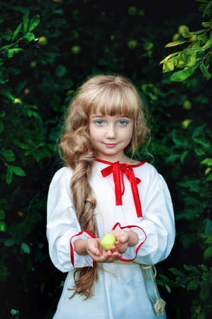 beautiful red-haired girl with a long beautiful braid, holding out a green Apple in her hand. Beauty of youthの写真素材