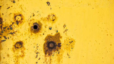 Round holes in the metal sheet. texture of a metal surface with cracked yellow paint and traces of rust.の写真素材