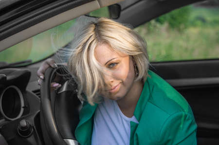close-up of a young female driver at the wheel. A blonde with blue eyes looks into the camera lens.の写真素材