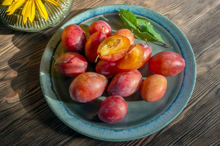 Ripe large juicy red plum lies in a beautiful plate on a wooden rustic table.