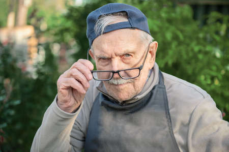 tired old man looks at his interlocutor, adjusts his glasses. The old man cant see very well without...