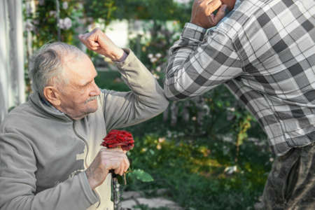 Elbow strike. A new greeting method to avoid the spread of the COVID-19 coronavirus. The old man and his son bump elbows instead of greeting him with a hug or handshake. Protecting the elderly from the virus.の写真素材