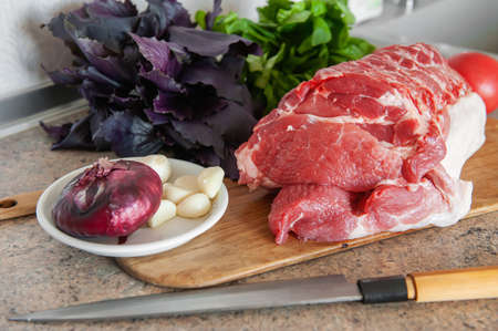 raw meat, a large piece of fresh pork on a chopping Board. A piece of pork with Basil, tomato and...