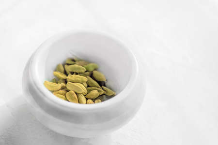 Raw organic cardamom pods are ready to use in a white stone mortar on a white background. Copy space.の写真素材