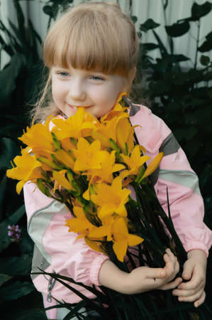 Funny red-haired girl with a bouquet of yellow lilies laughs. Portrait of a cheerful child.の写真素材