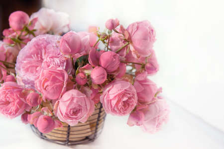 bouquet of pink English roses in a basket on a light table background. Close-up of rose buds, selective focus. Close up.の写真素材
