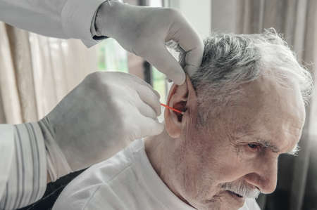 doctor cleanses the earwax of an elderly man. Geriatric care for the elderly.