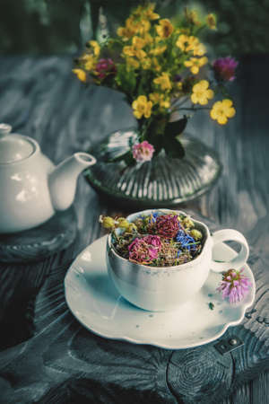 medicinal herbal tea with chamomile flowers and a bouquet of wild flowers in a beautiful Cup on a rustic wooden background. Rustic still life, authentic setting.の写真素材