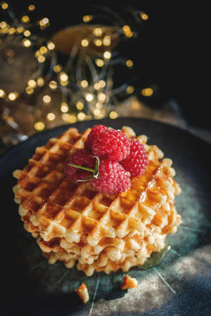 Sweet fresh Golden waffles. serve sweet Viennese waffles with fresh ripe raspberries on a beautiful plate with a garland background. Waffles on the holiday table.の写真素材