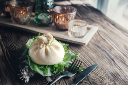 Burrato cheese on a lettuce leaf with appliances on a wooden table by the window. The table is decorated with candlesticks.の写真素材