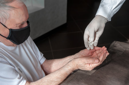 doctor's hand gives an old patient a pill. Gerontology service, nursing home. Unrecognizable people,...