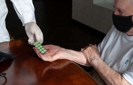 doctor's hand gives an old patient a pill. Gerontology service, nursing home. Unrecognizable people, part of the body.の写真素材