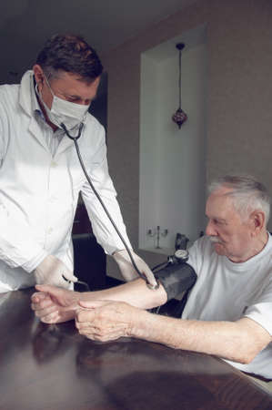 close-up of a doctor using a stethoscope on an elderly person's elbow to measure blood pressure. A...